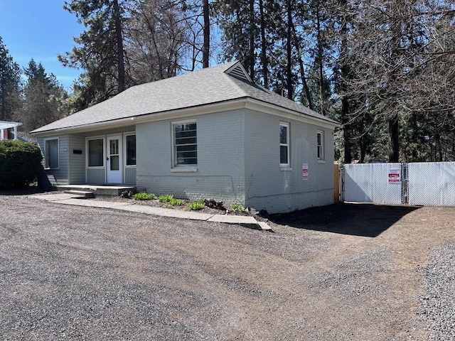 view of front facade with brick siding, fence, dirt driveway, and a shingled roof