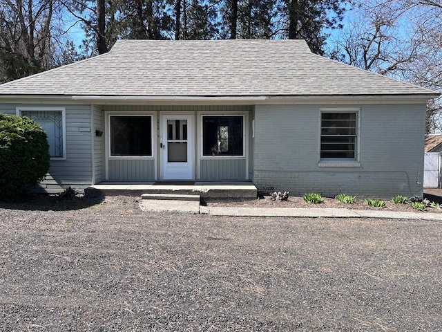 view of front of home with covered porch, a shingled roof, and brick siding