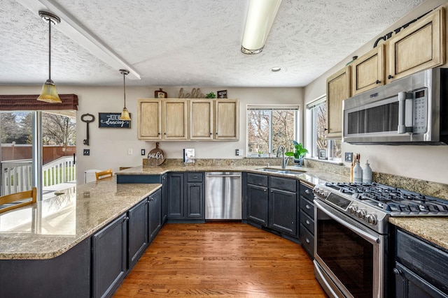 kitchen featuring a textured ceiling, stainless steel appliances, light wood finished floors, a sink, and hanging light fixtures