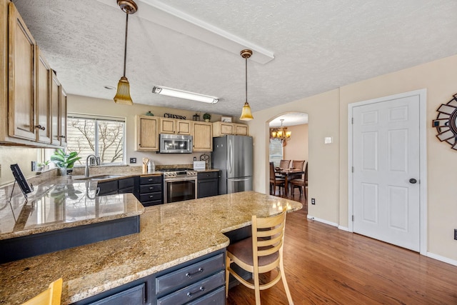 kitchen with dark wood-style flooring, a textured ceiling, stainless steel appliances, arched walkways, and a sink