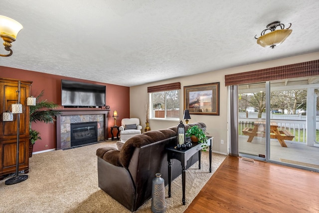 living room with visible vents, baseboards, a tiled fireplace, a textured ceiling, and wood finished floors