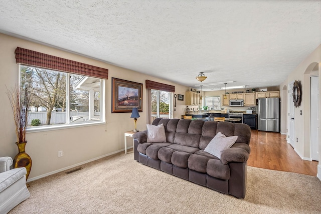 living area with a textured ceiling, baseboards, visible vents, and carpet floors