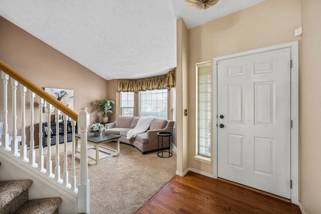 entrance foyer featuring a textured ceiling, vaulted ceiling, wood finished floors, stairs, and baseboards