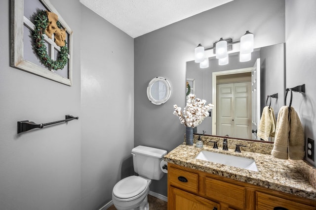 bathroom with toilet, a textured ceiling, vanity, and baseboards