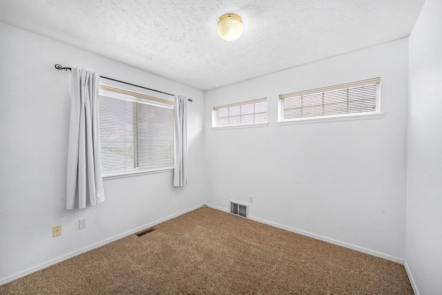 empty room featuring a textured ceiling, baseboards, carpet, and visible vents