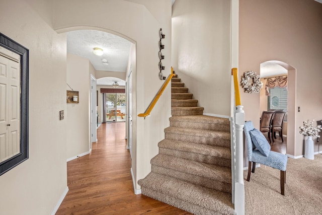 stairs with arched walkways, baseboards, and wood finished floors