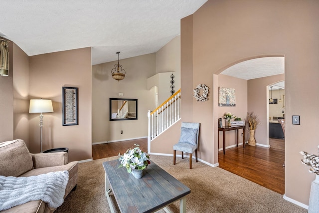 carpeted living area featuring high vaulted ceiling, arched walkways, stairway, and baseboards