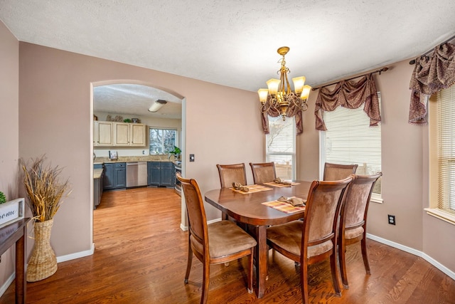 dining room featuring baseboards, arched walkways, a chandelier, a textured ceiling, and light wood finished floors