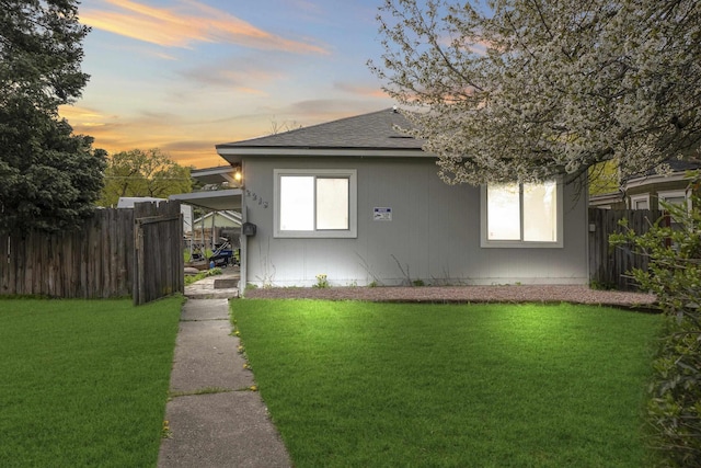 property exterior at dusk with fence, a yard, and a shingled roof