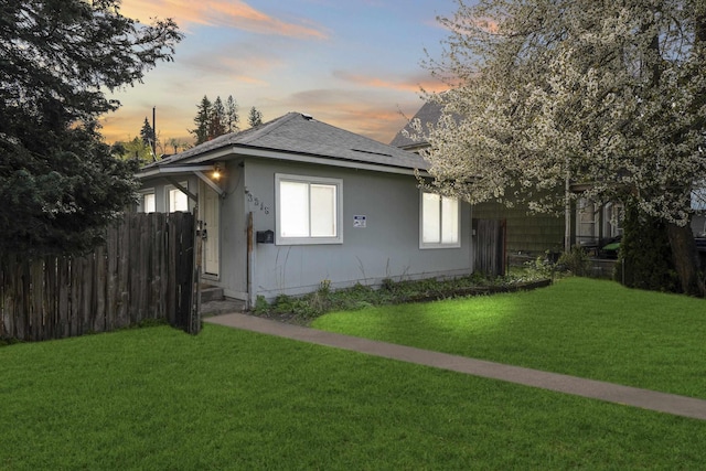 bungalow featuring fence, a lawn, and roof with shingles