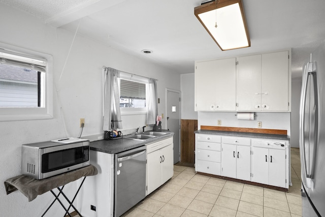 kitchen with stainless steel appliances, dark countertops, light tile patterned floors, a sink, and white cabinetry