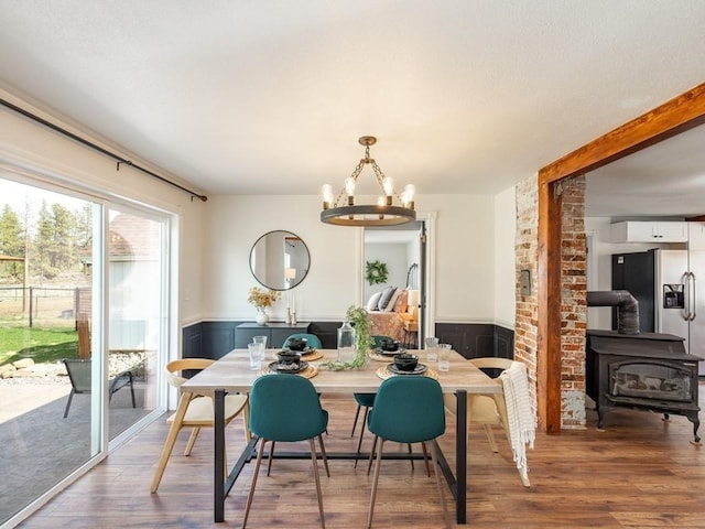 dining area featuring a wood stove, an inviting chandelier, a wainscoted wall, and wood finished floors