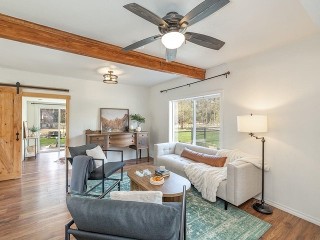 living area with baseboards, a barn door, a ceiling fan, beam ceiling, and wood finished floors