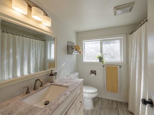 bathroom with toilet, wood finished floors, vanity, and baseboards