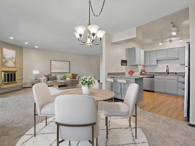 dining area featuring a stone fireplace, a chandelier, a textured ceiling, recessed lighting, and light carpet