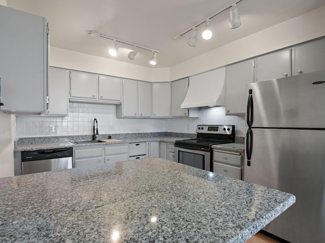 kitchen featuring dark stone countertops, custom exhaust hood, a sink, stainless steel appliances, and decorative backsplash