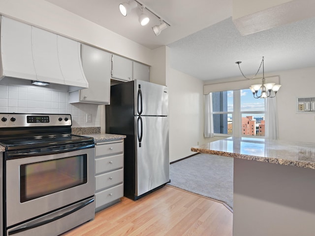 kitchen with custom exhaust hood, an inviting chandelier, light wood-type flooring, appliances with stainless steel finishes, and backsplash