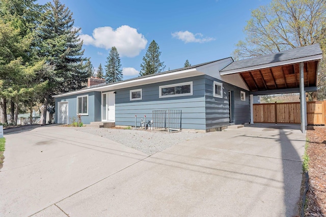 ranch-style house with a carport, driveway, fence, and a chimney