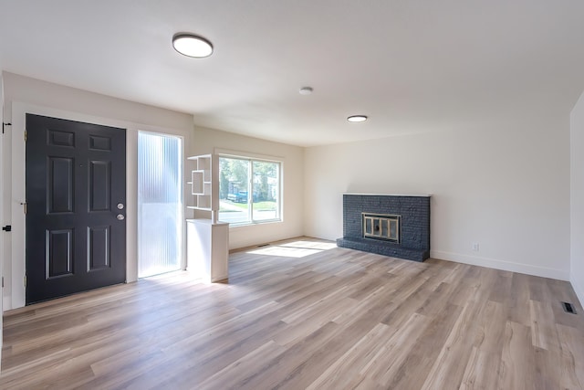 entrance foyer with visible vents, light wood-style flooring, a brick fireplace, and baseboards