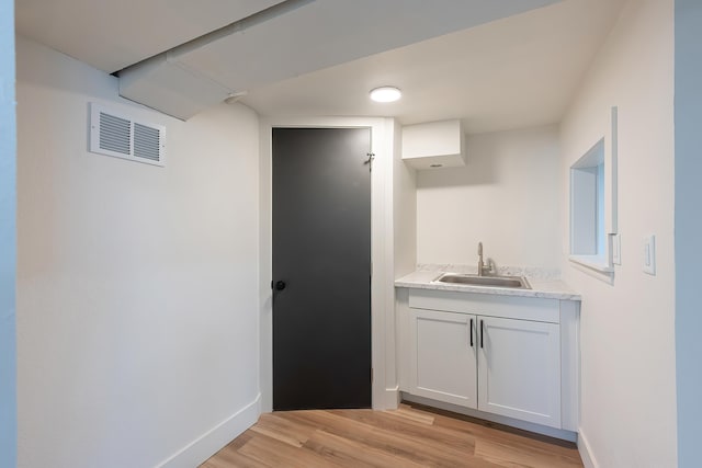 bar featuring light wood-style flooring, baseboards, a sink, and visible vents