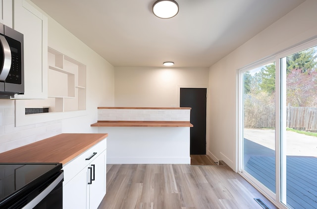 kitchen featuring butcher block countertops, stainless steel microwave, white cabinetry, and decorative backsplash