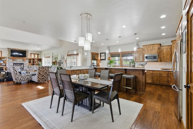 dining room with dark wood-style floors, a stone fireplace, and recessed lighting