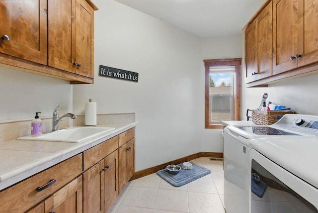 washroom with light tile patterned floors, a sink, washer and dryer, baseboards, and cabinet space