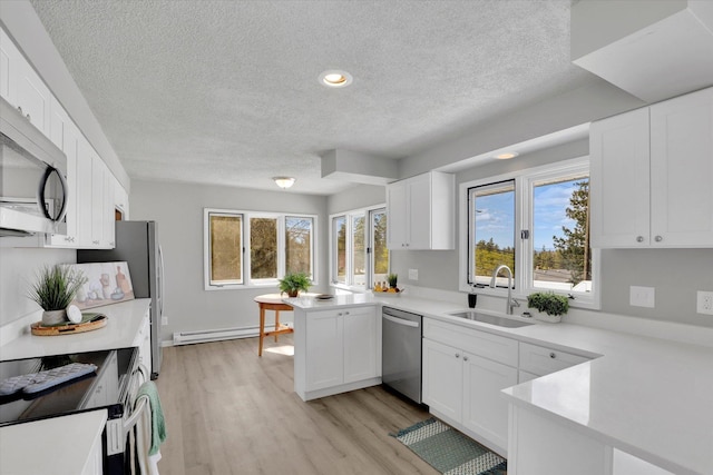 kitchen featuring a sink, a peninsula, a textured ceiling, baseboard heating, and stainless steel appliances