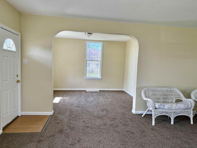 carpeted foyer with visible vents, baseboards, and arched walkways