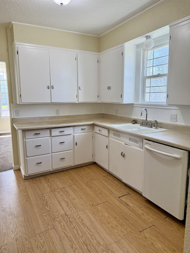 kitchen with light countertops, white cabinets, a wealth of natural light, white dishwasher, and a sink
