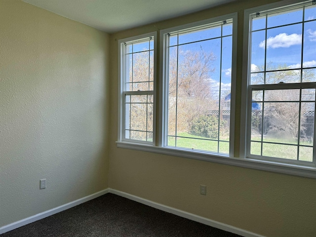 empty room featuring dark carpet, a textured wall, and baseboards