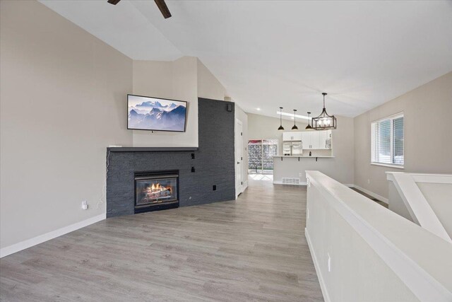 619 W Persimmon Ln, Spokane, WA 99224 - living room with light wood-style floors, ceiling fan with notable chandelier, a glass covered fireplace, visible vents, and vaulted ceiling