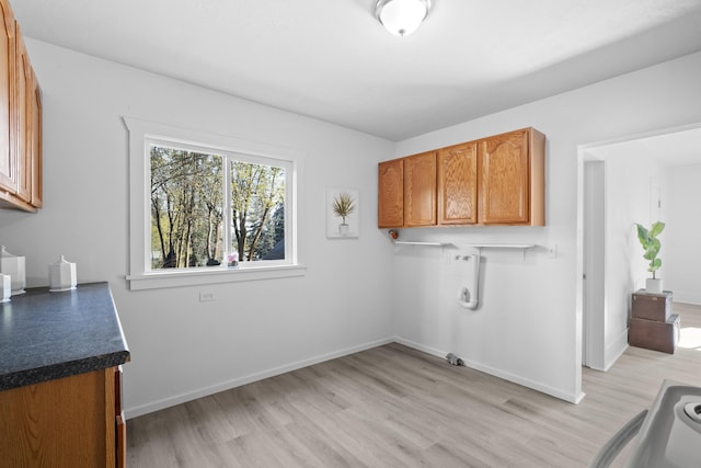 laundry area with light wood-type flooring, baseboards, and cabinet space