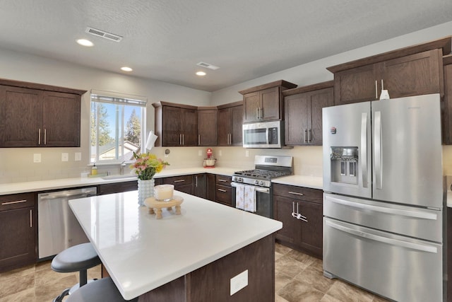 7407 E Beverly Ave, Spokane Valley, WA 99212 - kitchen featuring appliances with stainless steel finishes, dark brown cabinetry, light countertops, a kitchen bar, and a kitchen island