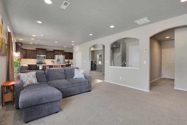 living room featuring light colored carpet, baseboards, recessed lighting, stairs, and arched walkways