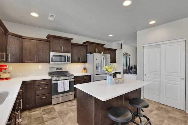 kitchen with stainless steel appliances, a breakfast bar, dark brown cabinets, a kitchen island, and light countertops