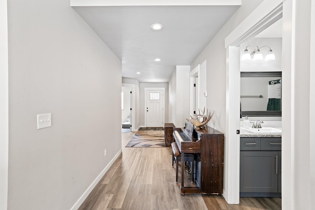 hall with recessed lighting, baseboards, a sink, and light wood-style floors