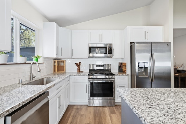 kitchen with lofted ceiling, stainless steel appliances, white cabinets, and a sink