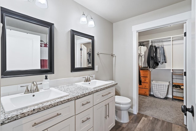 bathroom with double vanity, wood finished floors, toilet, and a sink