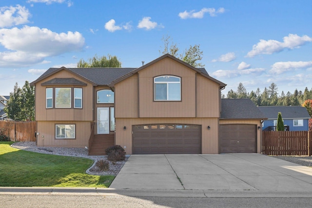 raised ranch featuring an attached garage, concrete driveway, fence, and a front lawn