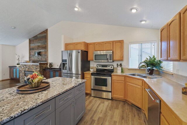 kitchen with light wood-style floors, a stone fireplace, appliances with stainless steel finishes, a sink, and lofted ceiling