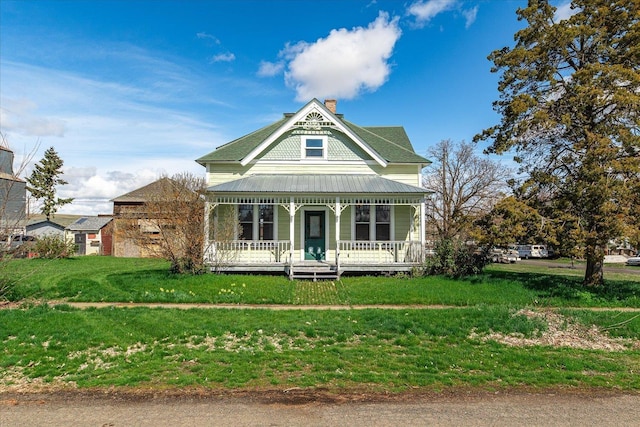 victorian-style house featuring a front yard, a porch, a chimney, and metal roof