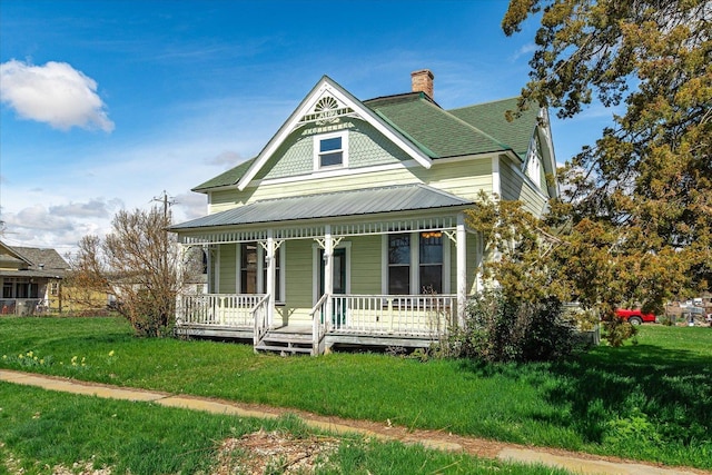 victorian-style house with roof with shingles, a front yard, a porch, and a chimney