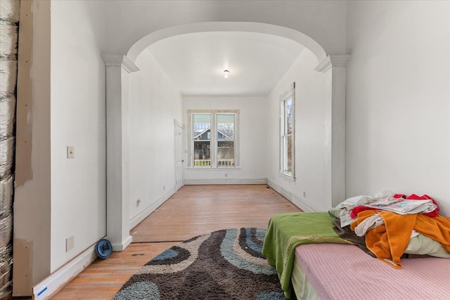 bedroom with baseboards, light wood finished floors, arched walkways, and decorative columns