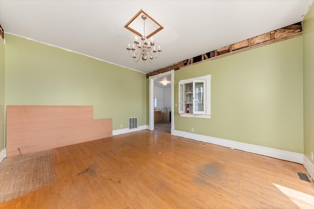 empty room with a notable chandelier, visible vents, baseboards, and wood finished floors