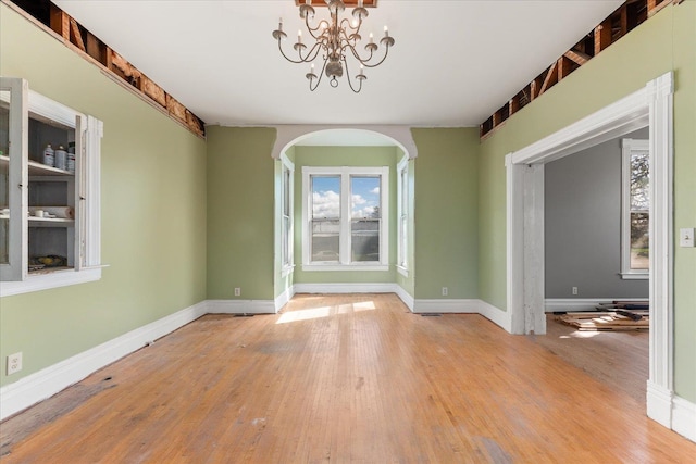 unfurnished dining area featuring a wealth of natural light, arched walkways, wood finished floors, and baseboards