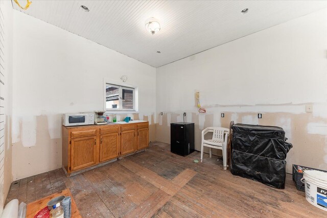 kitchen featuring white microwave, light countertops, brown cabinets, hardwood / wood-style floors, and lofted ceiling
