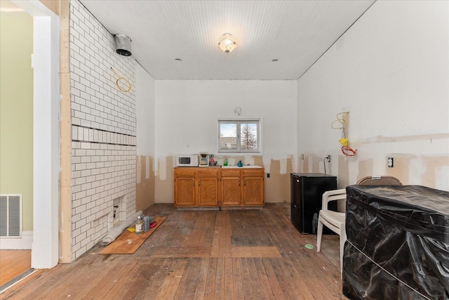 kitchen with brown cabinetry, a sink, wood-type flooring, and visible vents