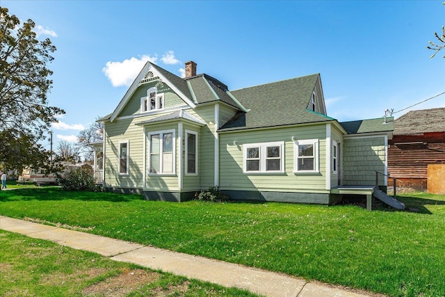 victorian house featuring a shingled roof, a chimney, and a front lawn