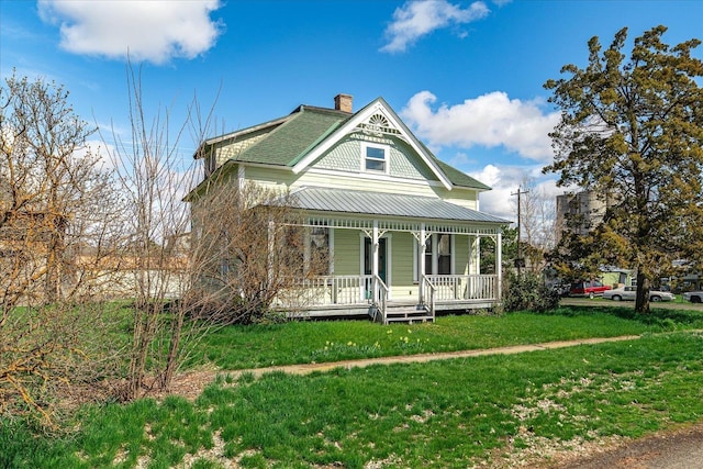 victorian-style house featuring a shingled roof, a chimney, a front lawn, and covered porch